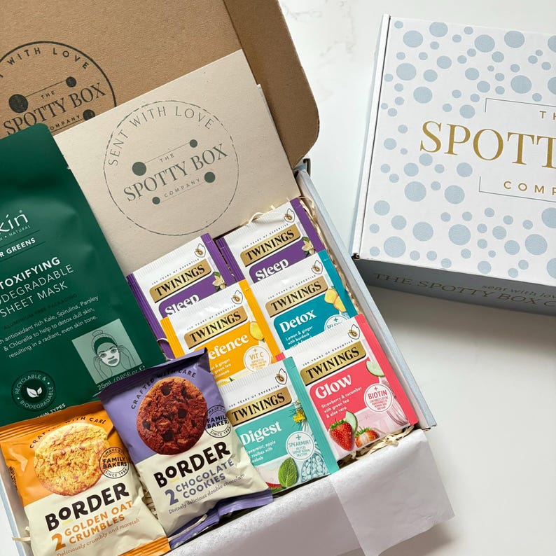 gift hamper containing 2 packs of border biscuits, 6 herbal/fruit tea bags and a sukin facemask with a nicely presented box in white with light blue polka dots and gold writing stating' the spotty box company'.