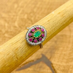 May include: A silver ring with a green oval gemstone surrounded by smaller pink and white gemstones.