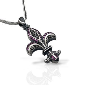 Op de afbeelding: Een zilverkleurige metalen hanger in de vorm van een fleur-de-lis, voorzien van ingewikkelde krulgravures en ingelegd met kleine, levendige magentakleurige steentjes. De hanger hangt aan een bijpassende zilverkleurige slangenketting.