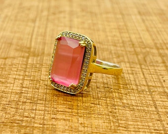 May include: A gold ring with a large pink gemstone surrounded by smaller clear gemstones.