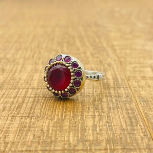 Peut inclure: Une bague en argent avec une grande pierre rouge ronde entourée de petites pierres violettes.