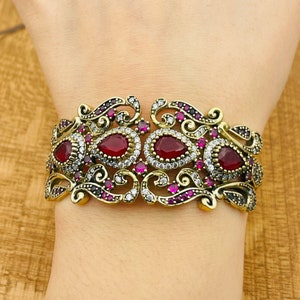 May include: A gold-tone bracelet with a filigree design and red and clear stones.