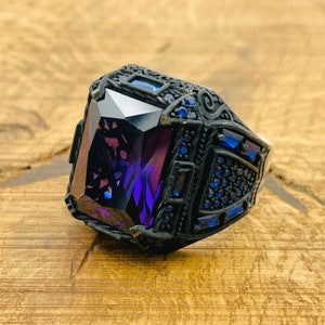 May include: A black silver ring with a large, faceted, purple gemstone surrounded by smaller blue gemstones.