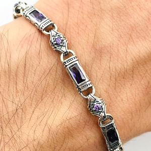 May include: Silver bracelet with rectangular and oval links, each adorned with a deep purple rectangular stone. The bracelet features intricate detailing and smaller purple stones, creating a striking contrast against the silver.