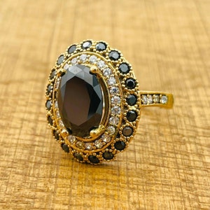 May include: A gold ring with a large black oval gemstone surrounded by a double halo of smaller white and black gemstones.