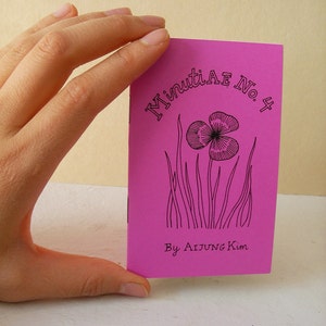 May include: A pink booklet with the title "Minutiae No. 4" and the text "By AIJUNG Kim". The cover features a black and white illustration of a flower with a stem and leaves.