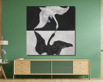 Op de afbeelding: Een vierkante muurkunstprint met een witte zwaan op een zwarte achtergrond boven een zwarte zwaan op een witte achtergrond. De twee vogels zijn zo geplaatst dat hun snavels elkaar in het midden raken, wat een symmetrisch contrast vormt.