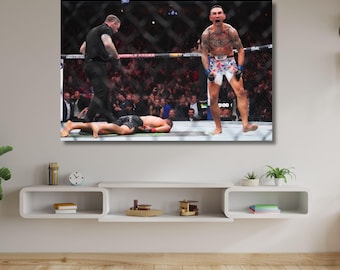 May include: A rectangular wall art print depicting a mixed martial arts fight inside a chain-link cage. One fighter stands shouting with arms raised, wearing white and floral patterned shorts, while another fighter lies on the mat nearby.