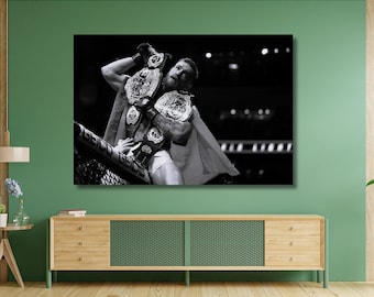 May include: A black and white wall art print depicting a fighter standing inside a cage, holding two championship belts aloft. The athlete wears athletic shorts and a draped flag, with the word GEICO visible on the cage structure in the foreground.
