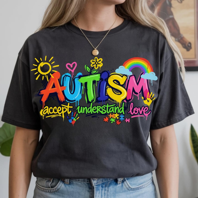 May include: Dark gray t-shirt with the word "AUTISM" in colorful graffiti-style lettering. The shirt also features the phrases "accept understand love", a rainbow, sun, hearts, flowers, and puzzle pieces.