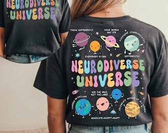 Może przedstawiać: Ciemnoszara koszulka z napisem "NEURODIVERSE UNIVERSE" w kolorowych, falistych literach. Tył przedstawia grafikę planet i gwiazd z frazami takimi jak "Myśl inaczej" i "Świętuj wszystkie umysły."