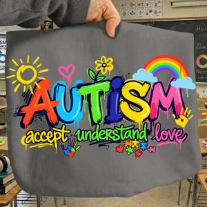 May include: Gray fabric with the word "AUTISM" in colorful graffiti-style lettering, accompanied by "accept understand love." The design includes a rainbow, sun, hearts, flowers, handprints, and puzzle pieces.