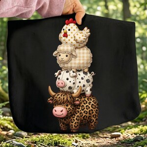 Peut inclure: Sac fourre-tout noir avec une illustration empilant des animaux de la ferme : une poule, un mouton, un cochon et une vache. La poule et le mouton ont un motif à carreaux, le cochon a des taches noires et la vache a un imprimé léopard.