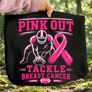Peut inclure: Un article en tissu noir avec un motif rose représentant un joueur de football américain en position de départ avec un ballon. Le texte indique PINK OUT TACKLE BREAST CANCER. Un grand ruban de sensibilisation rose et un ballon rose sont visibles.