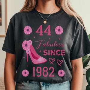 Peut inclure: T-shirt gris foncé avec un motif rose célébrant un 44e anniversaire. Le motif comprend le chiffre "44", les mots "Fabulous Since 1982", un escarpin, des cœurs et des motifs floraux.