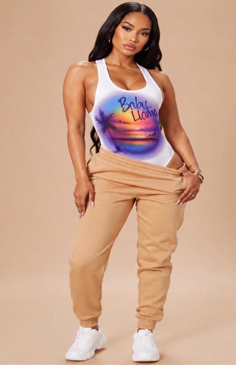 May include: A white racerback bodysuit featuring a colorful airbrushed sunset graphic with palm trees and the text Baby Llama, paired with tan sweatpants and white sneakers. The bodysuit has a scoop neckline and a fitted silhouette.