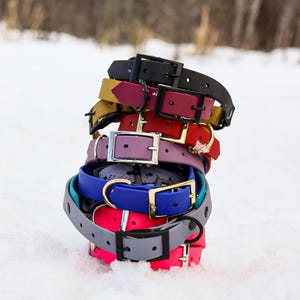 May include: A stack of colorful dog collars in various colors, including black, red, purple, blue, and gray. The collars are made of durable rubber and have metal buckles.