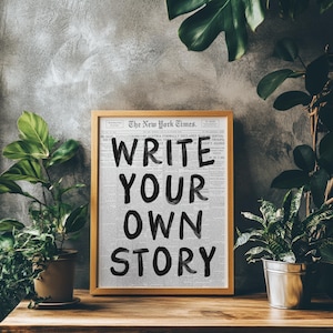 May include: A framed print of a newspaper clipping with the text "WRITE YOUR OWN STORY" in black marker on a white background. The newspaper is The New York Times.