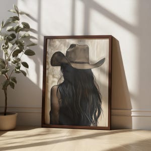 May include: A framed painting of a woman with long dark hair wearing a brown cowboy hat. The background is a light brown color.