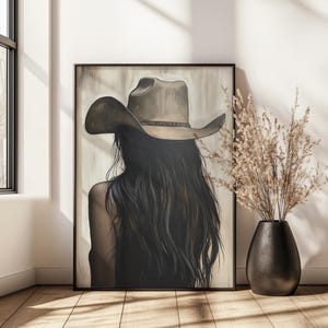 以下が含まれることがあります： 茶色のカウボーイハットをかぶった、長い黒髪の女性を描いた絵画。女性は鑑賞者から背を向けており、背中は鑑賞者に向けられている。背景は薄い茶色である。