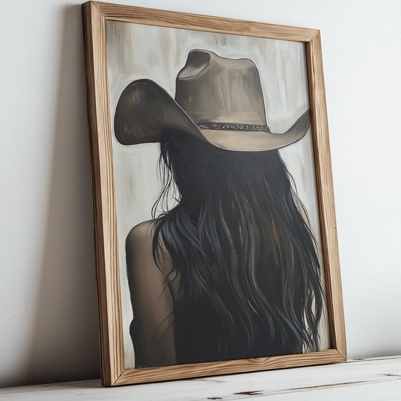 May include: A painting of a woman with long dark hair wearing a brown cowboy hat. The painting is framed in a light brown wood frame.
