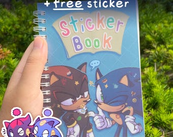 May include: A spiral-bound sticker book with the text "Reusable Stickerbook + free sticker". The cover features a cartoon illustration of two characters. The words "Sticker Book" are displayed on the cover. A sticker of two additional characters is in the lower left corner.