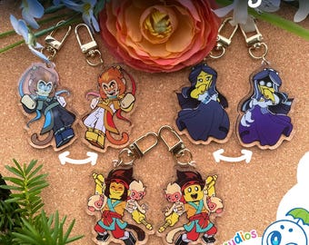 May include: A collection of acrylic keychains featuring reversible designs of animated characters. The keychains display various figures in colorful outfits with gold-toned metal clasps. The text Reversible Designs is visible at the top.