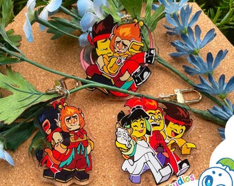 May include: Three clear acrylic keychains featuring colorful cartoon character illustrations. One shows two figures embracing, another depicts two characters standing back-to-back, and the third shows three characters running together.