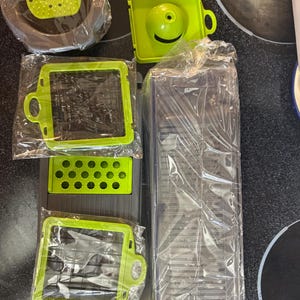 May include: A set of green and gray plastic kitchen tools for slicing and dicing vegetables. The set includes a mandoline, a grater, and a container for storing the sliced vegetables.