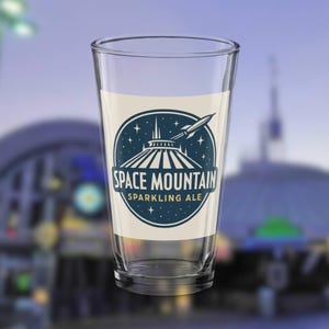 以下が含まれることがあります： 「Space Mountain Sparkling Ale」のラベルが付いた透明なパイントグラス。ラベルには、スペースマウンテンのアトラクション、ロケット、テキスト「SPACE MOUNTAIN SPARKLING ALE」の青と白のグラフィックが描かれています。