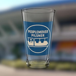 Könnte beinhalten: Ein klares Pilsner-Bierglas mit einem blauen Band, das den weißen Text "PEOPLEMOVER PILSNER" und eine weiße Grafik eines PeopleMover-Fahrzeugs zeigt. Das Glas ist leer.