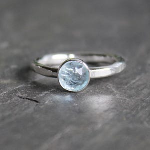 May include: A white ceramic mug with a black handle and the text "But First, Coffee" in a bold, black font. The mug is set against a blurred background, suggesting a cozy setting. The mug appears to be approximately 4 inches tall.