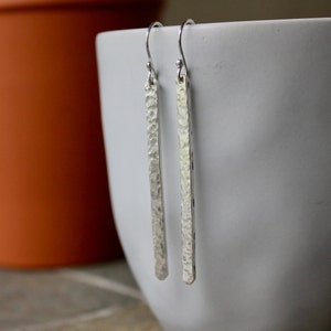 May include: A pair of silver hammered bar earrings. The earrings are long and thin, with a textured surface.