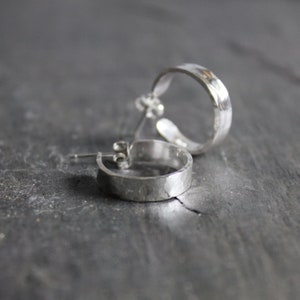 May include: A pair of silver hoop earrings with a hammered texture. The earrings are simple and elegant.