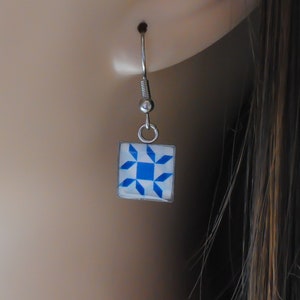 May include: A pair of silver earrings with a blue and white geometric pattern. The earrings are square shaped and have a simple design.