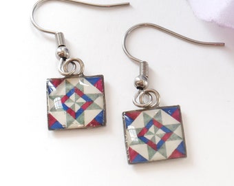 May include: A pair of silver earrings with a white, blue, and red geometric pattern. The earrings are square shaped and have a silver hook.