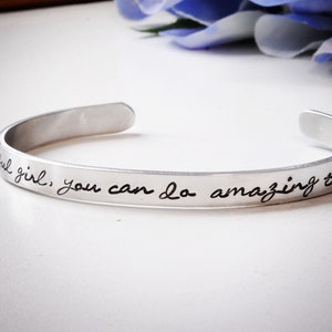 May include: A silver bracelet with the inscription "Beautiful girl, you can do amazing things".