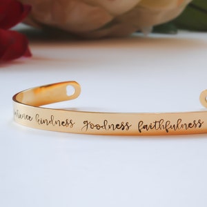 May include: Gold-toned bangle bracelet with the words "patience kindness goodness faithfulness gentleness" engraved on the band.