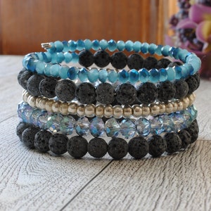 May include: A stack of bracelets featuring blue and silver beads, with a layer of black lava rock beads.