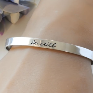 May include: A silver bangle bracelet with the words "be still" engraved on it.