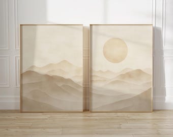 May include: Two framed landscape art prints. One features a mountain range, the other a sun over a mountain range. The artwork is in shades of beige and brown, with a minimalist aesthetic. The frames are gold.