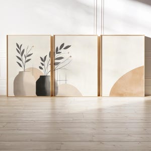 May include: A set of three framed wall art prints featuring abstract compositions. The first two prints display dark gray botanical illustrations in vases against a cream background. The third print shows a large, solid tan semi-circle shape.
