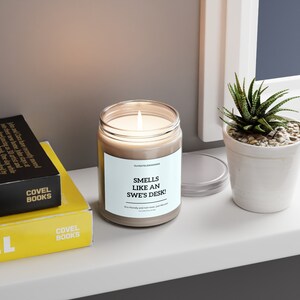 Pode incluir: Uma vela de vidro castanho com um rótulo branco que diz "Smells like an Swe's Desk!"  Eco friendly e não tóxico, como o verdadeiro.