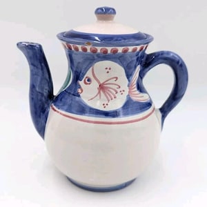 May include: A white ceramic teapot with a blue and red fish design. The teapot has a lid and a handle.
