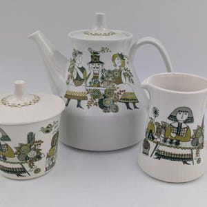 May include: A white ceramic tea set featuring a teapot, creamer, and sugar bowl. Each piece is decorated with a repeating pattern of figures in dresses and hats, with green and gold floral accents. The teapot has a lid and a curved spout.