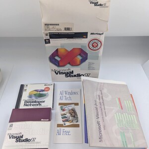 May include: A Microsoft Visual Studio 97 software package including a large white box with a red and purple infinity graphic, a Microsoft Developer Network CD case, a purple and white box, a promotional pamphlet, and a Microsoft Visual J++ manual.
