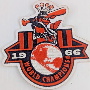 May include: Embroidered patch featuring a baseball-playing bird mascot with a bat, atop a baseball-themed globe. The patch is in black, orange, and white, with the text "1966 World Champions".