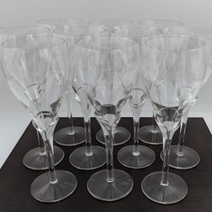 May include: A set of twelve clear crystal wine glasses. Each glass has a slender stem with a decorative design and a round base. The glasses are arranged on a dark surface.