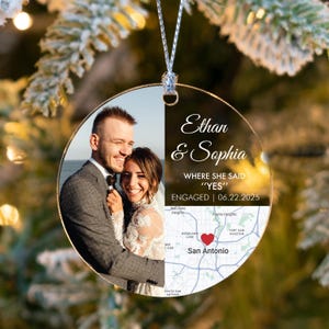 May include: A clear, round Christmas ornament with a photo of a smiling couple. The ornament includes the names "Ethan & Sophia", the text "WHERE SHE SAID YES", the engagement date, and a map of San Antonio.