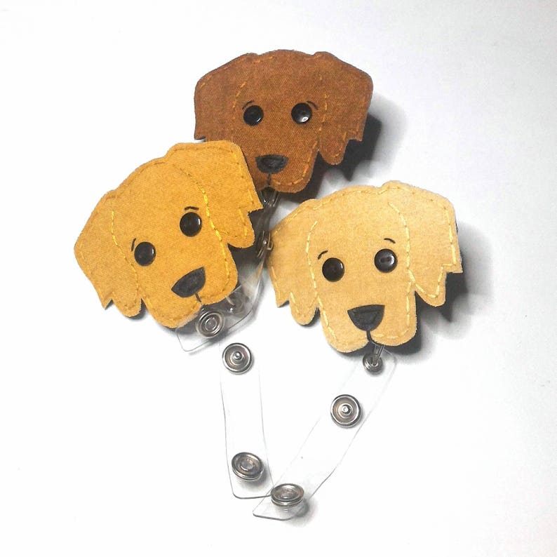 May include: Three felt dog badge holders with clear retractable reels. The dogs are brown, yellow, and light brown with black eyes and noses.